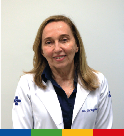 Mulher branca, loira, de cabelos lisos na altura do ombro e que veste uma camisa azul escura e um jaleco branco com a marca do SUS no braço direito; do Hospital da Criança de Brasília José Alencar no braço esquerdo, e o nome bordado na parte da frente. Isis Maria, diretora técnica do HCB sorri para o registro.